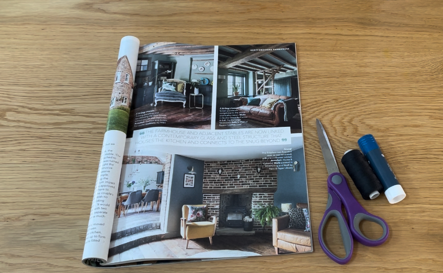 Open magazine showing living spaces, purple scissors, glue and black thread lying on wooden table