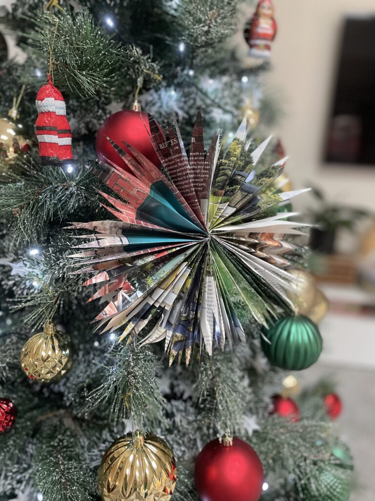 Coloured paper star hanging off Christmas tree with green, red and golden baubles