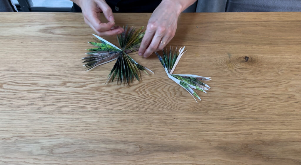 Woman arranging pieces of folded paper into star shape and connecting them with black string on wooden table