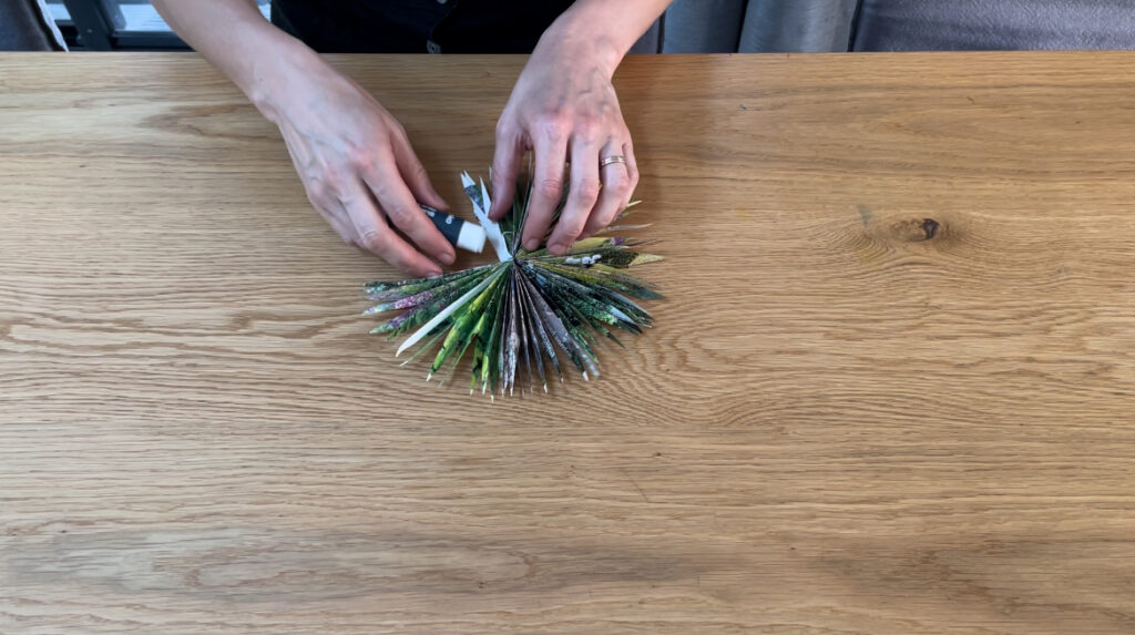 Woman using glue stick to connect edges of paper star on wooden table