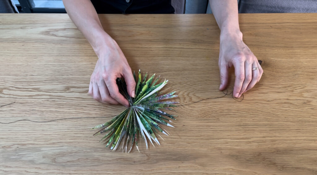 Woman tying black string around green paper star on wooden table