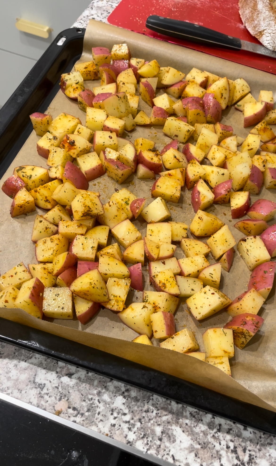 Red herbed potato chunks on baking tray