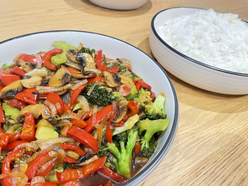 Vegetable stir fry and rice in who white bowl on wooden table