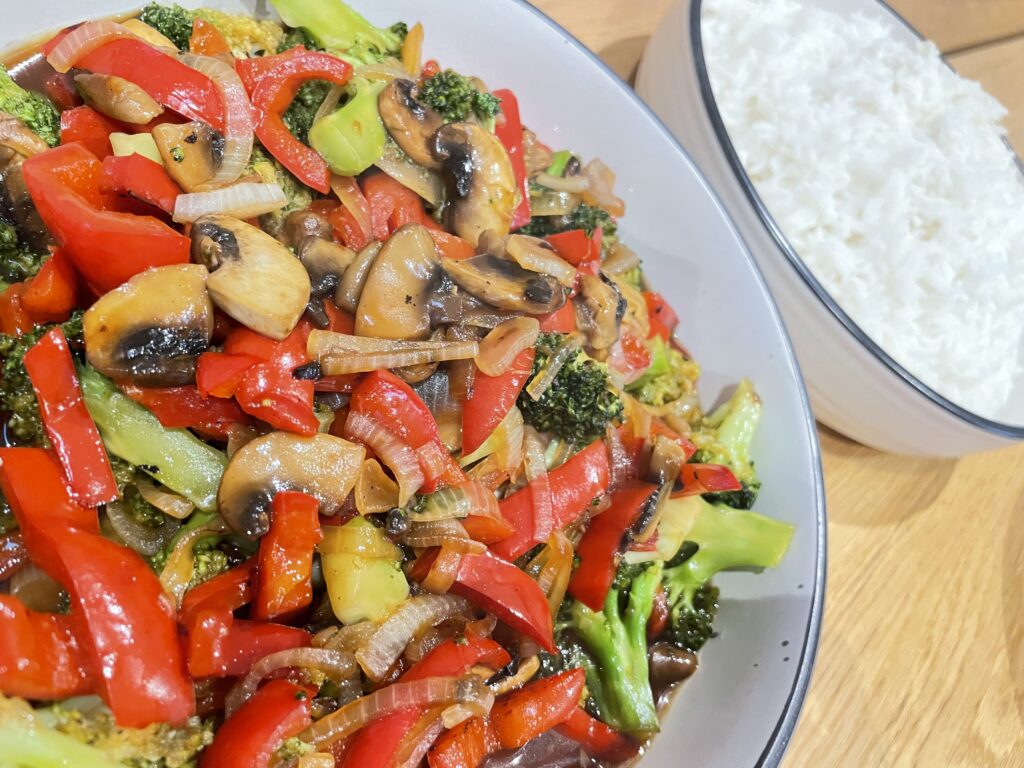 Two bowls on wooden table, one filled with white rice, the other filled with vegetable stir fry