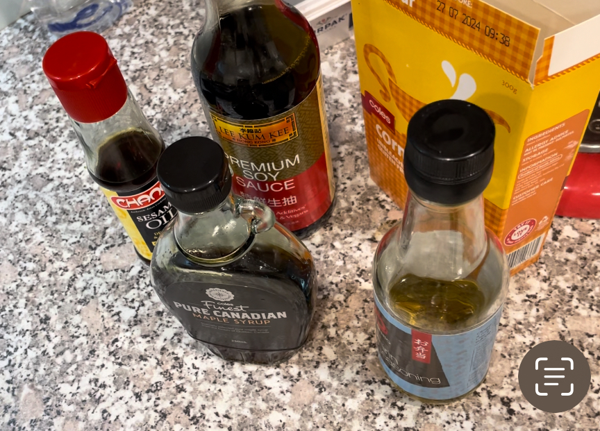 Selection of condiments standing on granite bench top, including soy sauce, maple syrup and corn flour