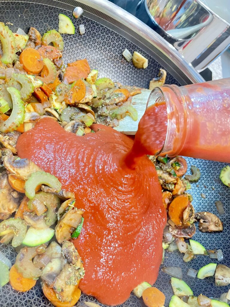 Red sauce pouring into frying pan with vegetables