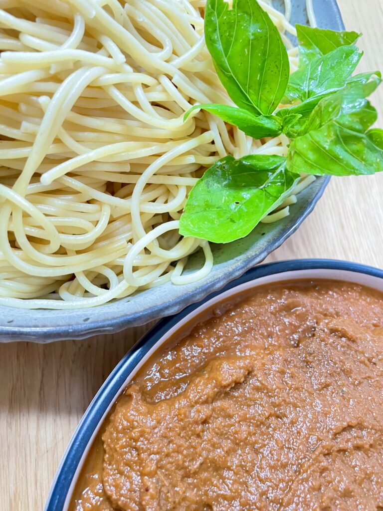 Bowl filled with cooked spaghetti decorated with basil next to bowl filled with pasta sauce