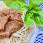 White bowl with blue dots filled with spaghetti dish and basil