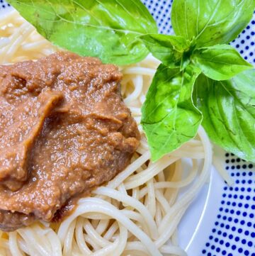 White bowl with blue dots filled with spaghetti dish and basil