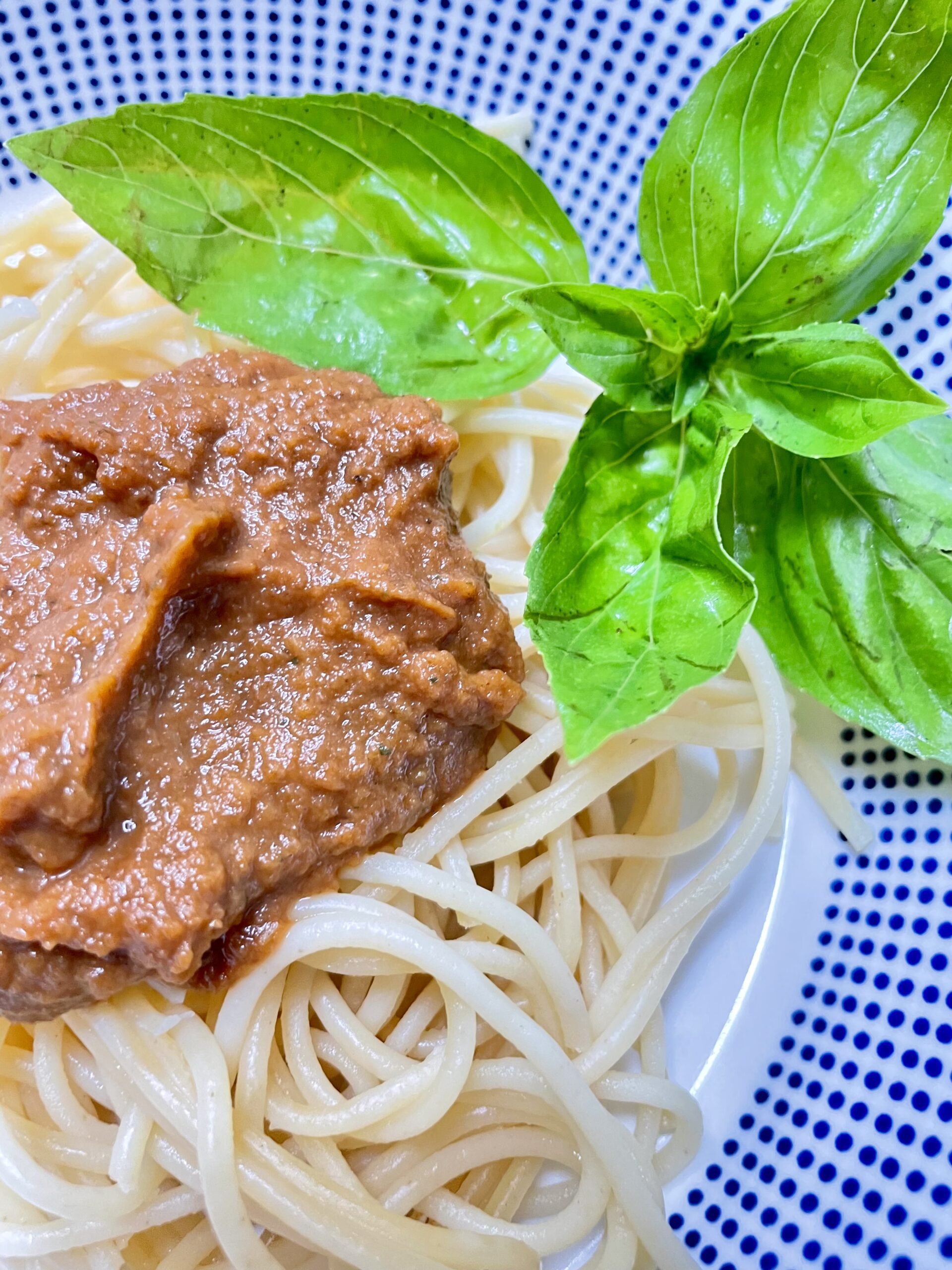 White bowl with blue dots filled with spaghetti dish and basil