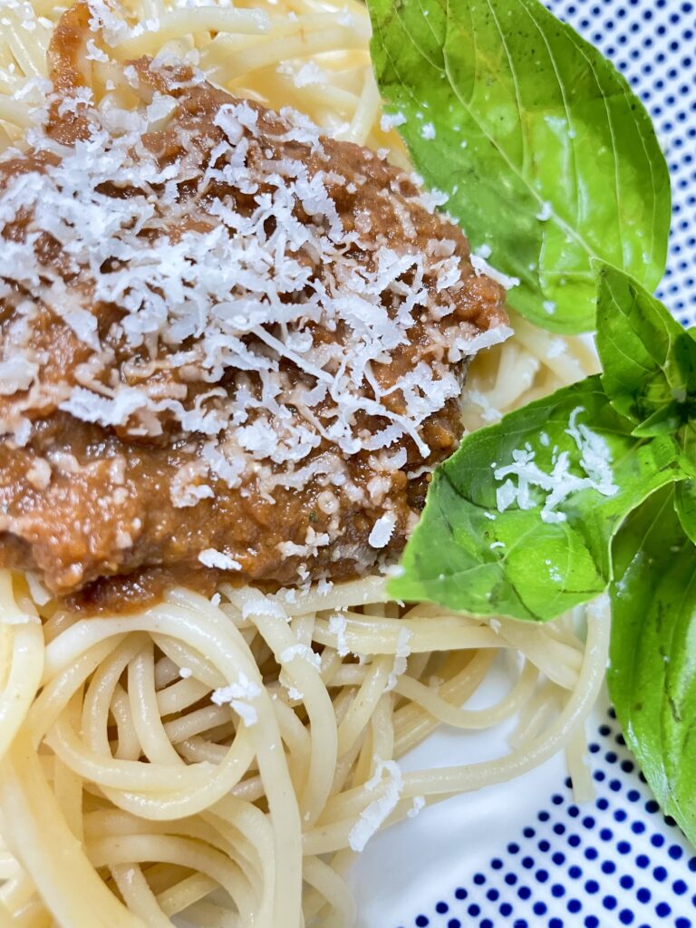 White bowl with blue dots filled with spaghetti and sauce, topped with parmesan cheese and basil