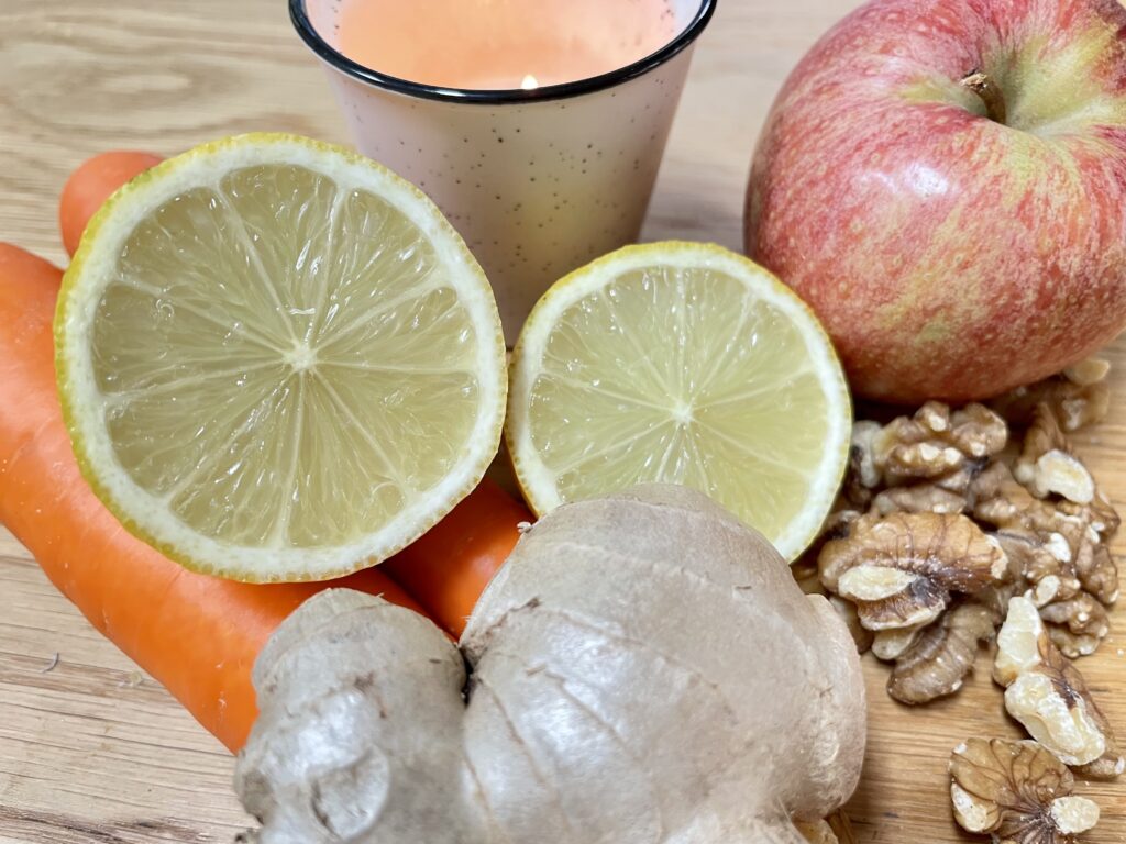 Carrot, apple, lemon, ginger and walnuts next to candle on wooden table