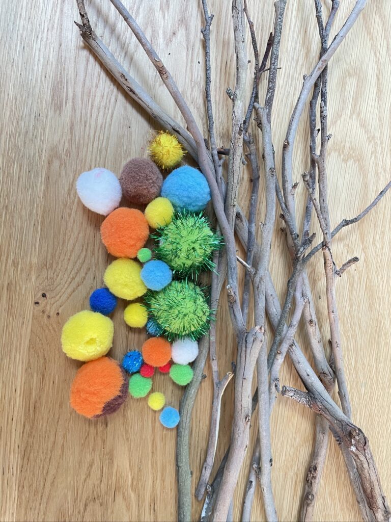 Dry twigs and colourful pom poms of various sizes laying on wooden table