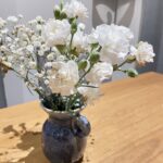 White flowers in simple blue vase sitting on wooden farmhouse table in living room