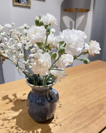 White flowers in simple blue vase sitting on wooden farmhouse table in living room