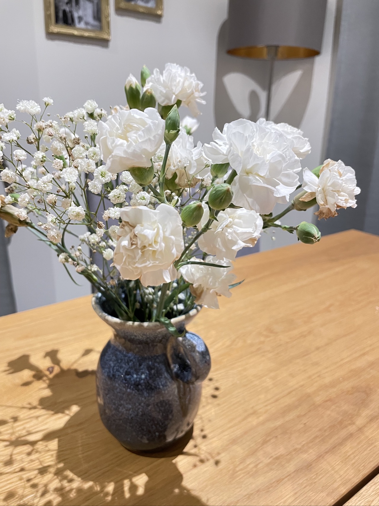 White flowers in simple blue vase sitting on wooden farmhouse table in living room