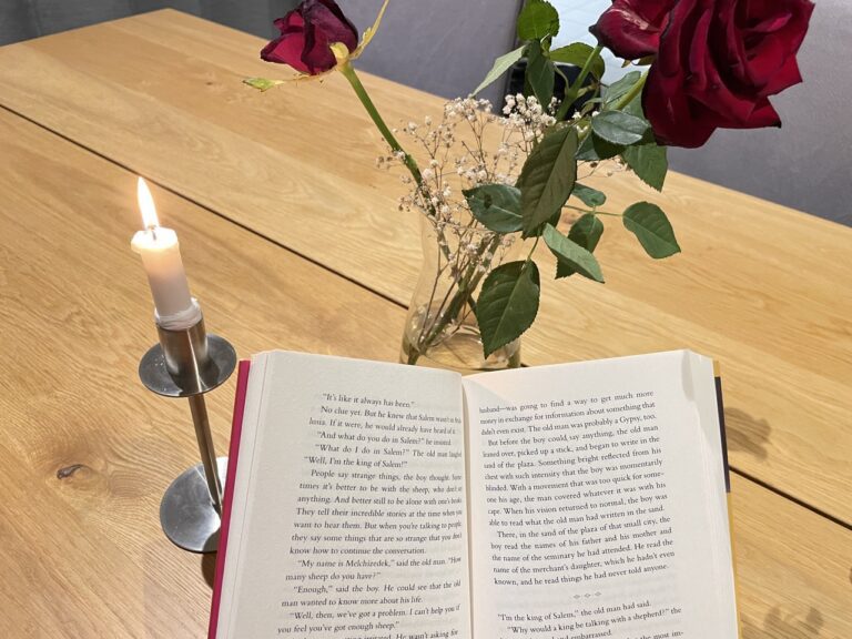 Open book for reading in front of candle and flowers