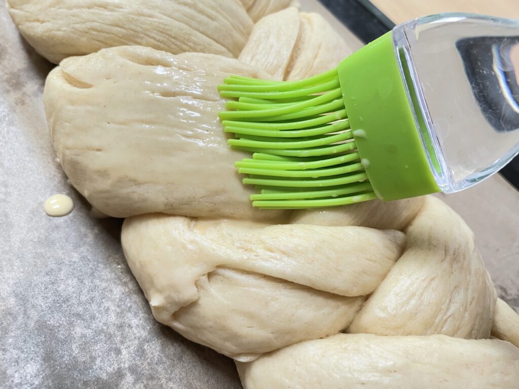 Green silicone brush brushing over braided dough