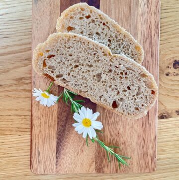 Wooden board with two slices of whole wheat rye sourdough and white flowers