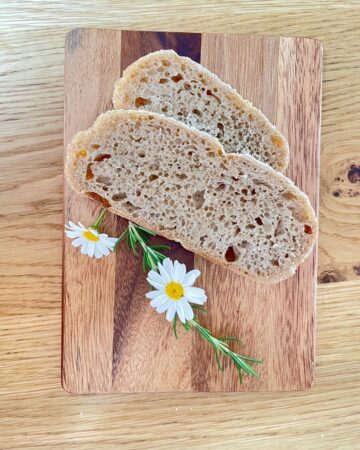 Wooden board with two slices of whole wheat rye sourdough and white flowers