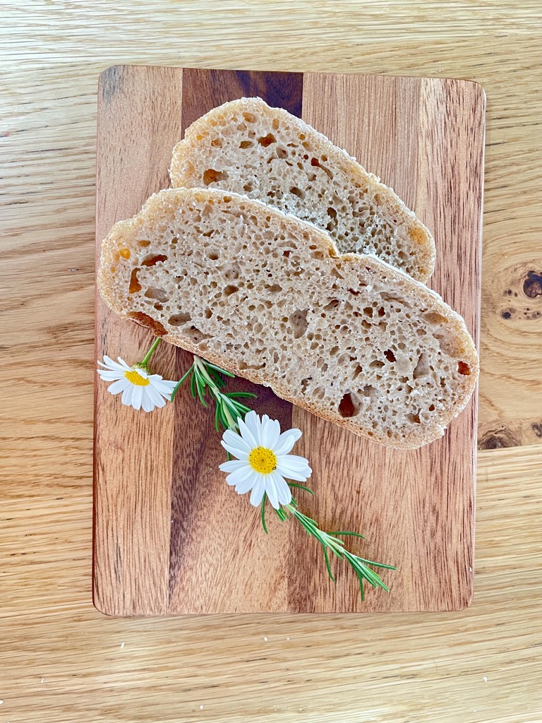 Wooden board with two slices of whole wheat rye sourdough and white flowers