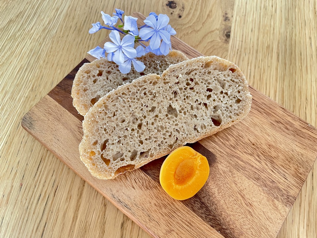 Two slices of rye bread arranged on wooden board with flowers and half an apricot