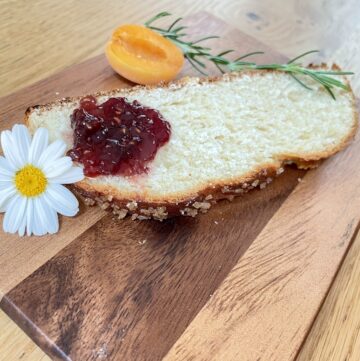 Slice of Hefezopf on wooden chopping board with jam, flower and apricot