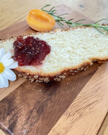 Slice of Hefezopf on wooden chopping board with jam, flower and apricot