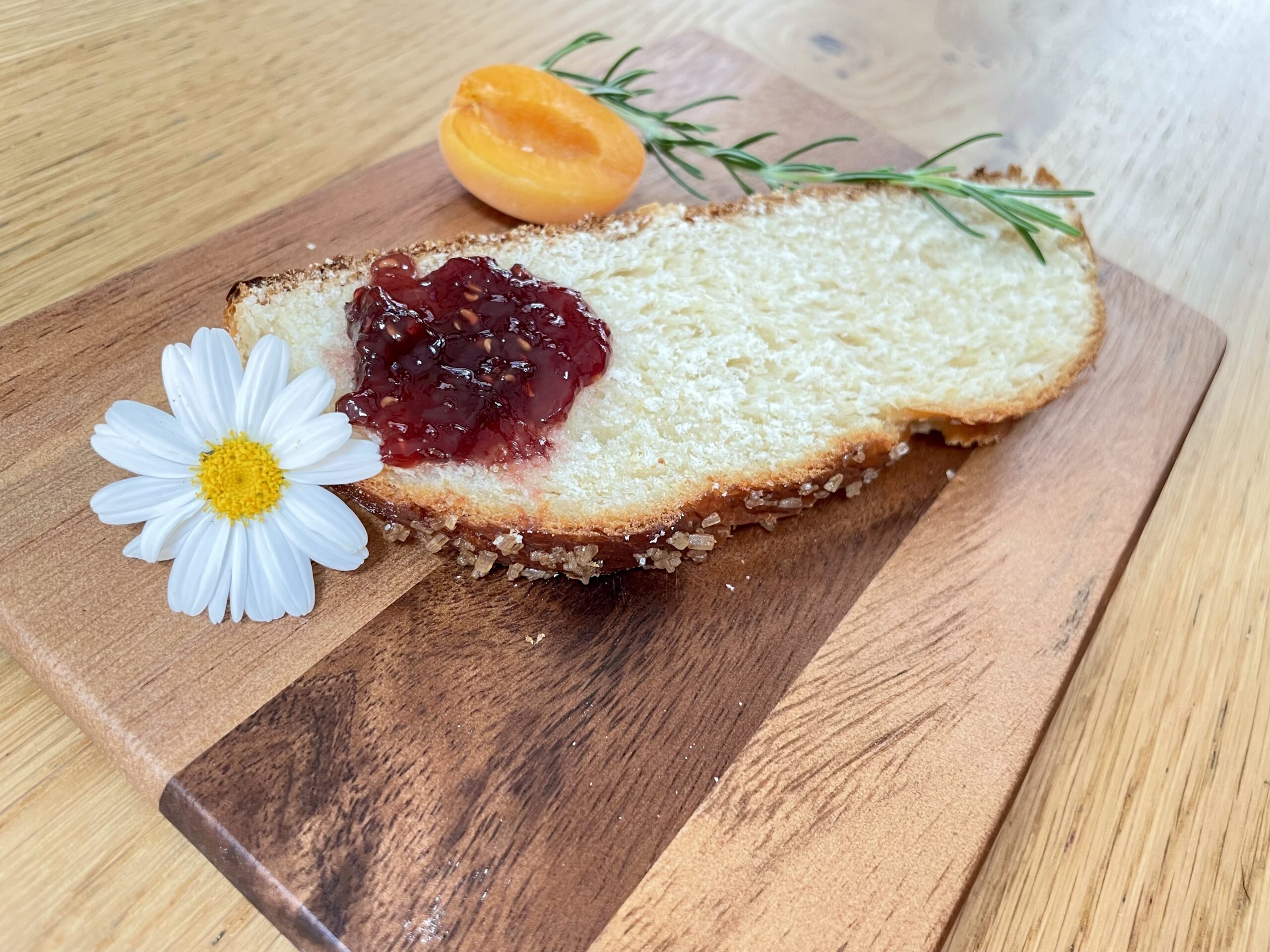 Slice of Hefezopf on wooden chopping board with jam, flower and apricot