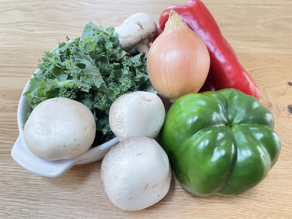 Bowl of kale and mushrooms next to capsicum and onion