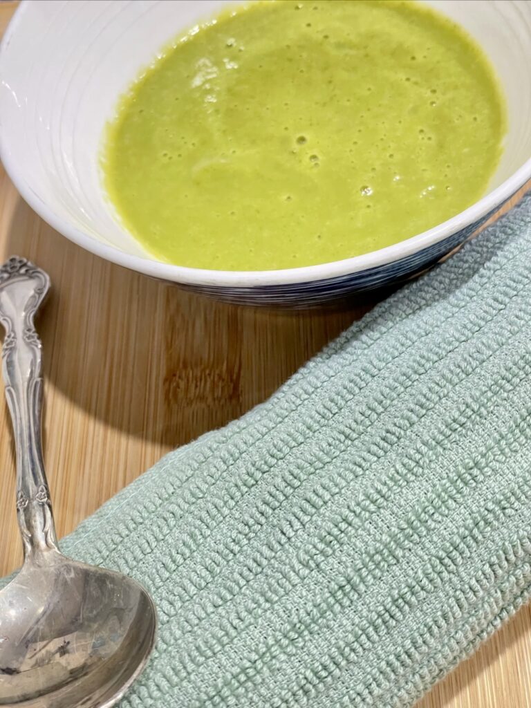 White bowl on wooden table with green soup, spoon and napkin