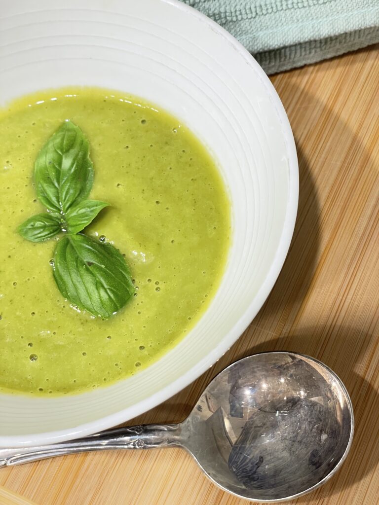 Bowl of green soup with silver spoon sitting on wooden background