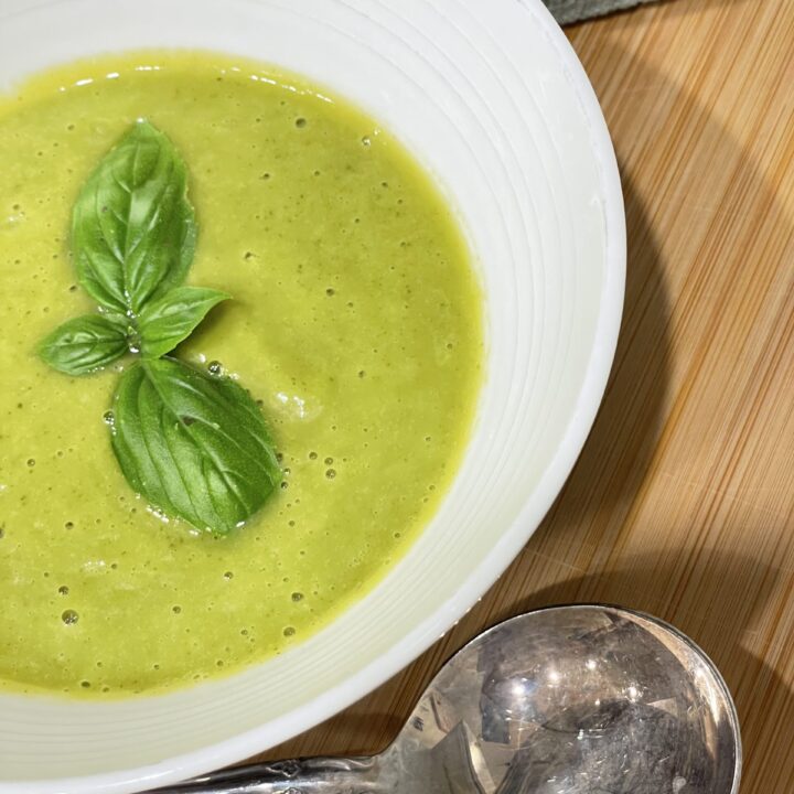 Bowl of green soup with silver spoon sitting on wooden background