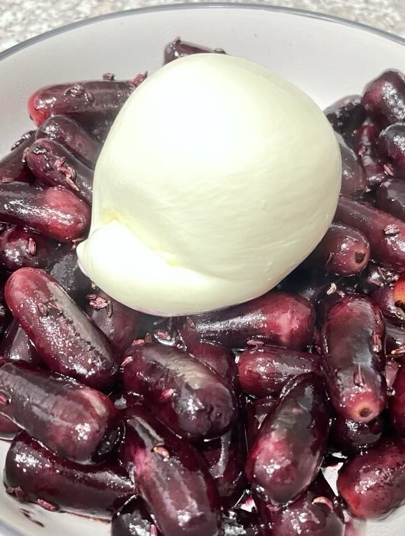 Close up shot of burrata sitting on grilled red grapes