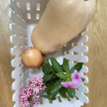 White basket with butternut squash, onions and pink flowers On wooden table