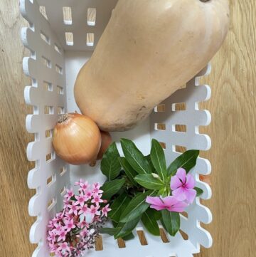 White basket with butternut squash, onions and pink flowers On wooden table