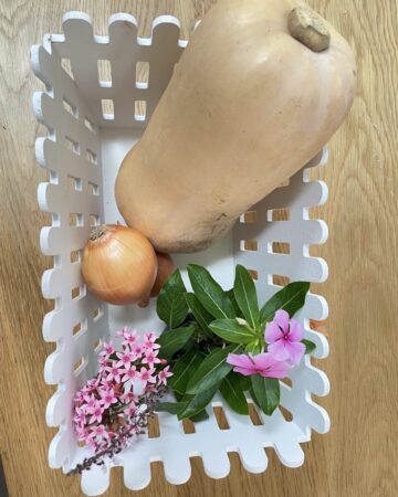 White basket with butternut squash, onions and pink flowers On wooden table