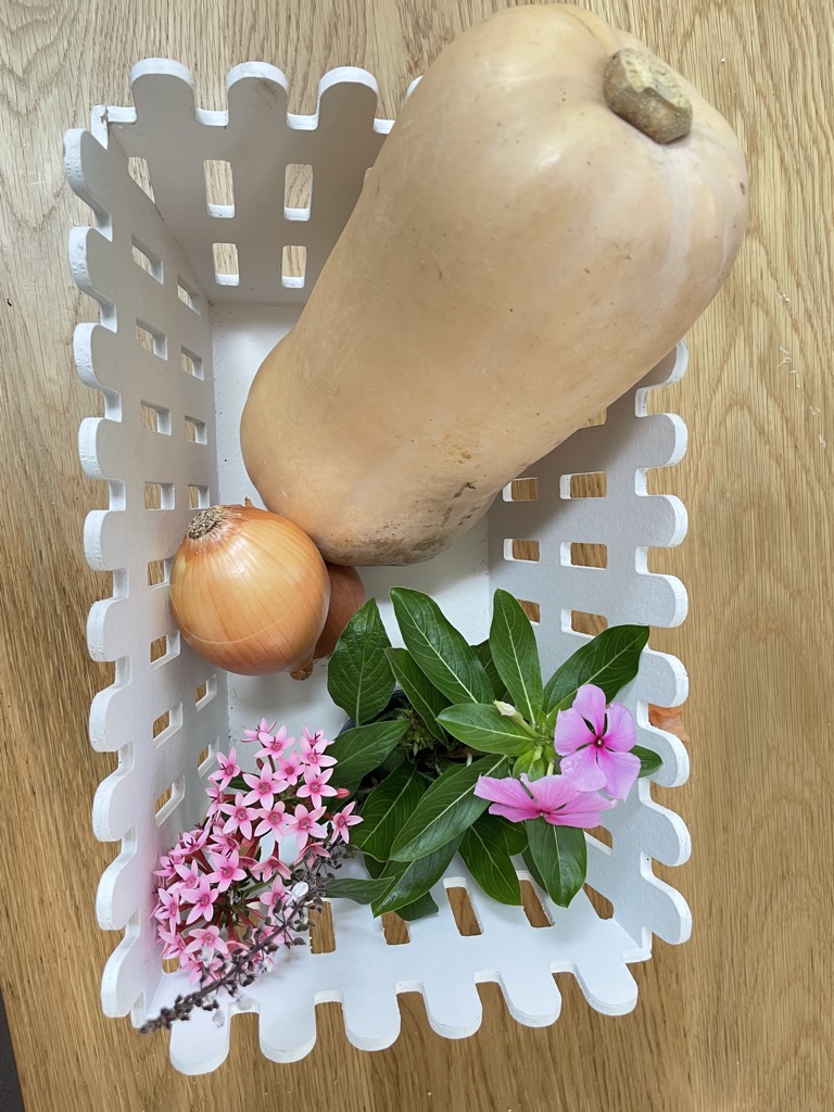 White basket with butternut squash, onions and pink flowers On wooden table