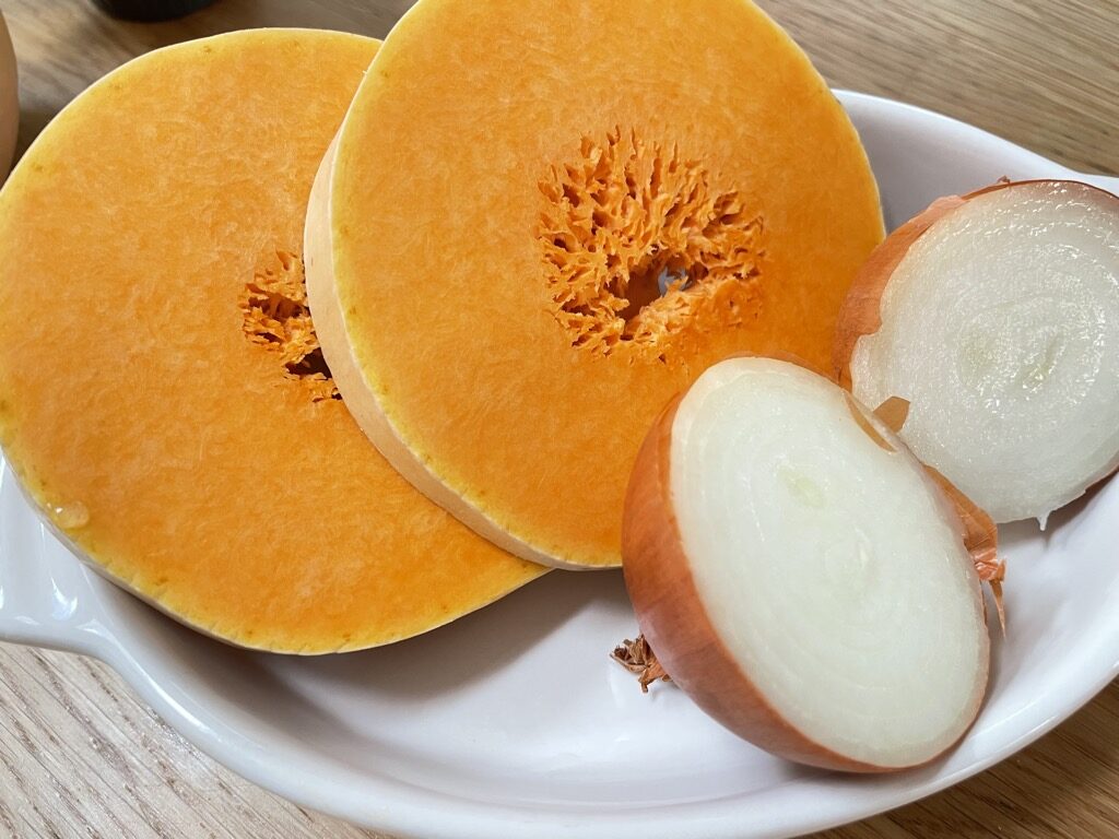 White bowl filled with sliced butternut squash and half onions