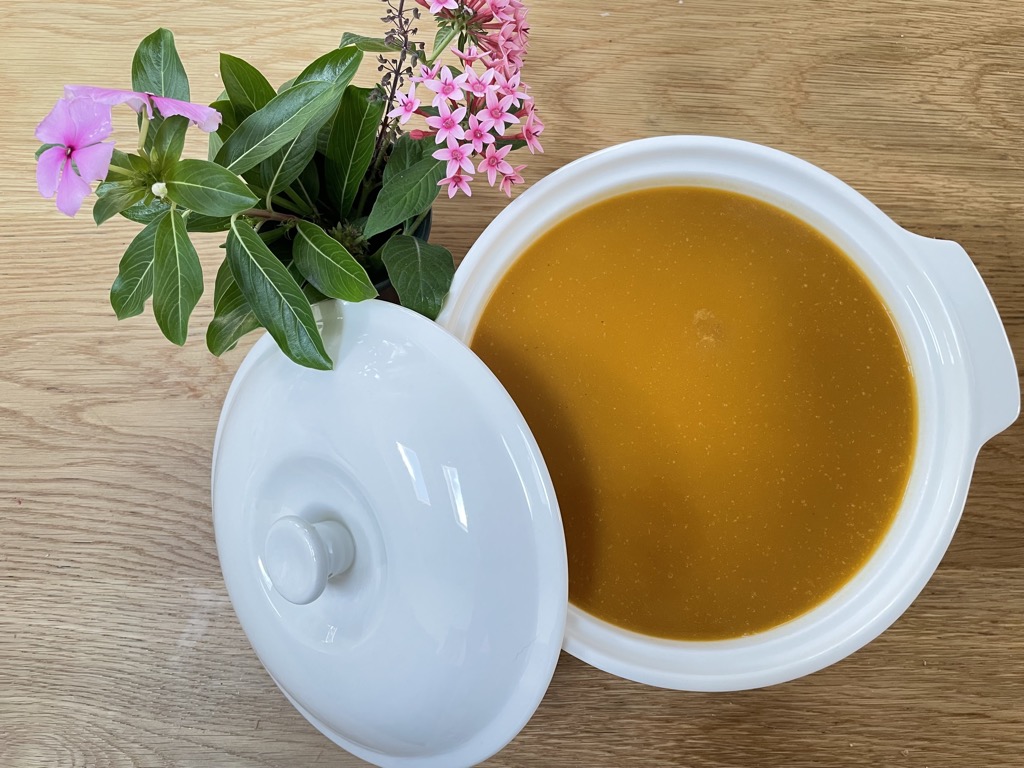 Wooden table with white boal of butternut squash soup and vase of flowers