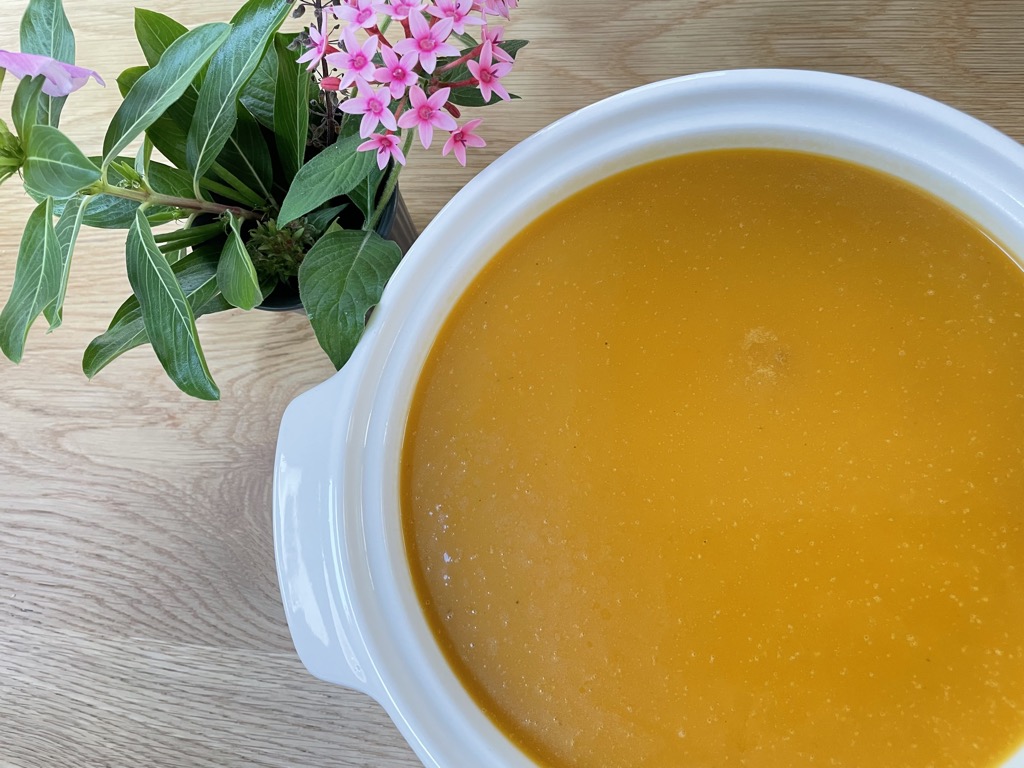 White serving bowl of butternut squash soup with vase of flowers