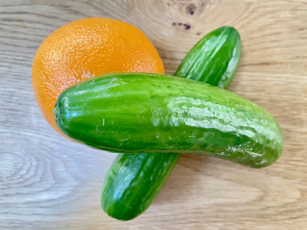 Two lebanese cucumbers and an orange on a wooden table