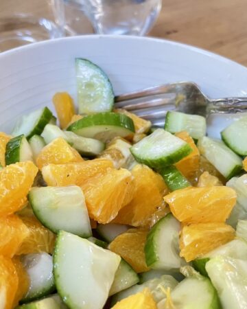 Fresh Cucumber and Orange Salad In a white bowl with silver fork