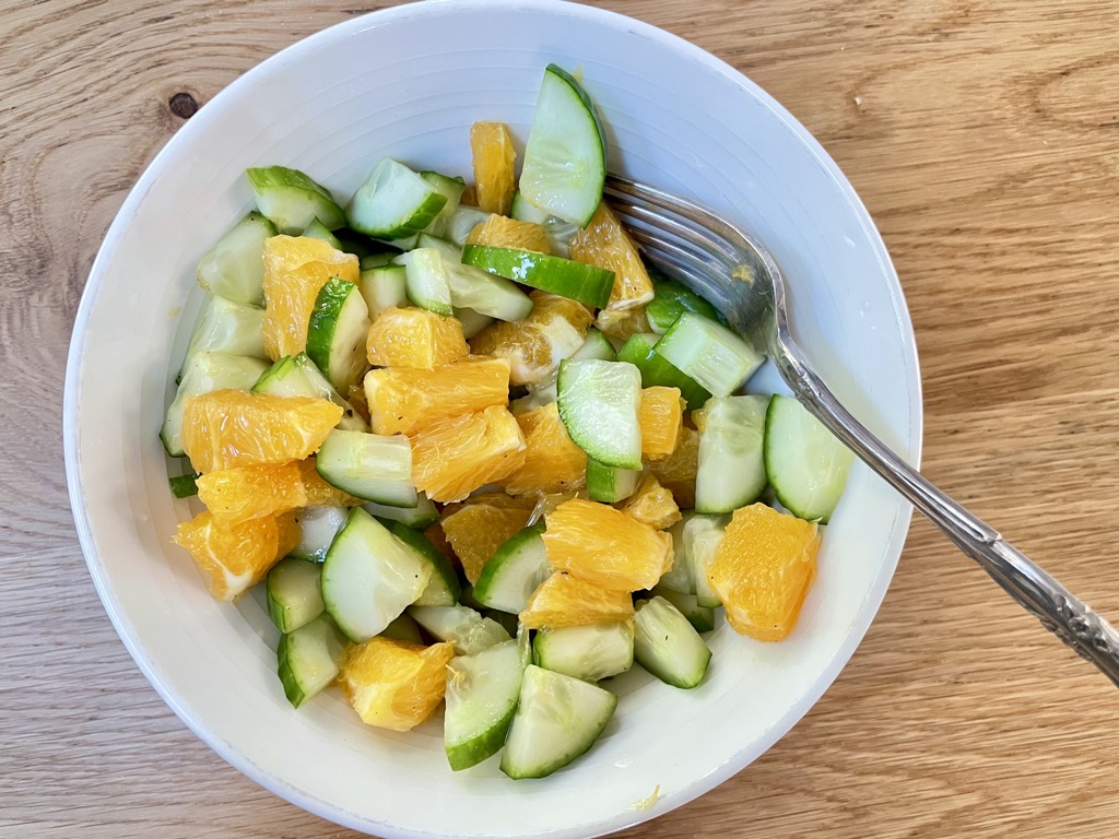 Fresh Cucumber and Orange Salad In white bowl on wooden table