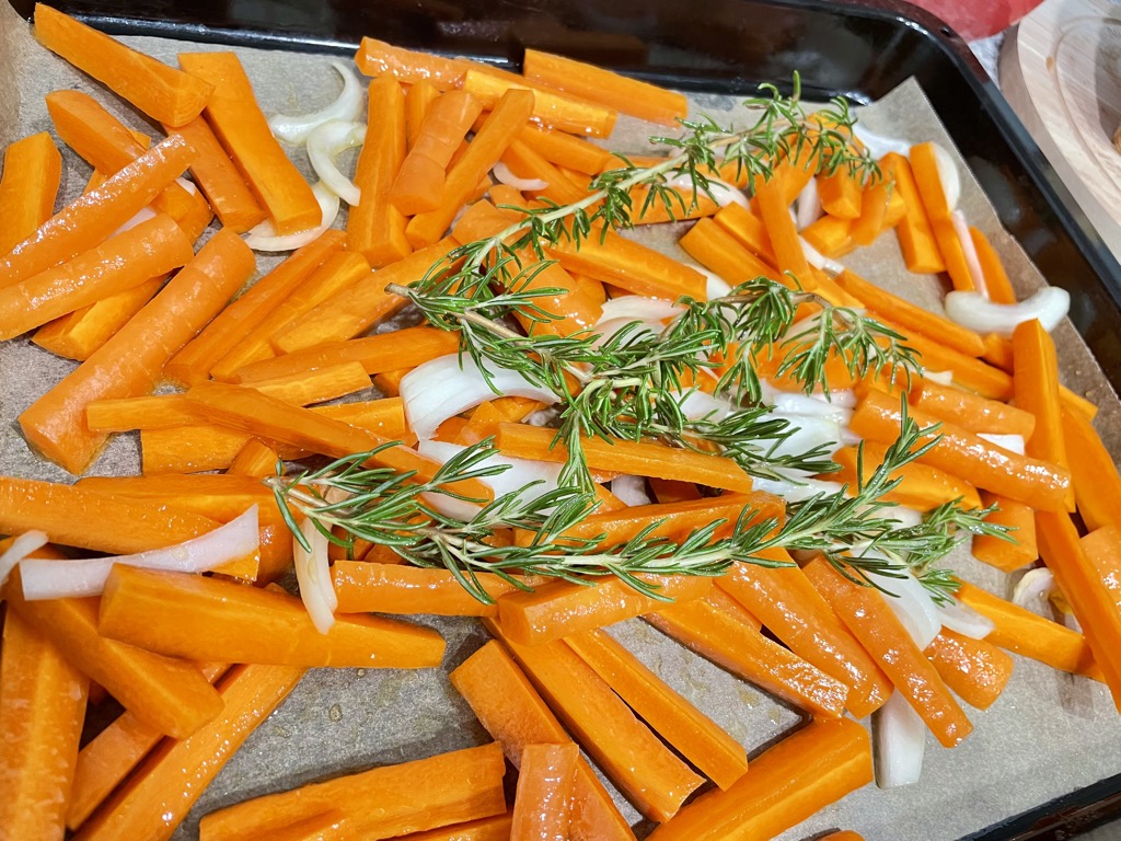 Roasting tray of fresh carrot sticks, onions and rosemary