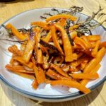 White bowl with black rim, filled with roasted carrots and rosemary On wooden table