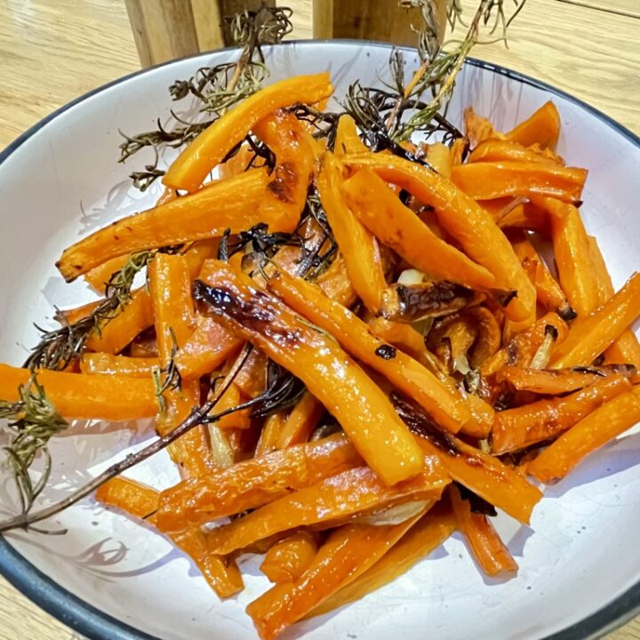 White bowl with black rim, filled with roasted carrots and rosemary