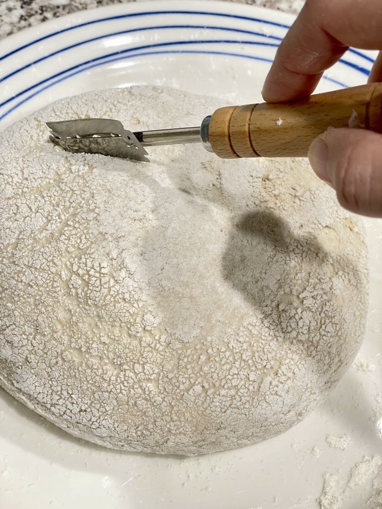 Hand holding bread lame scoring sourdough loaf