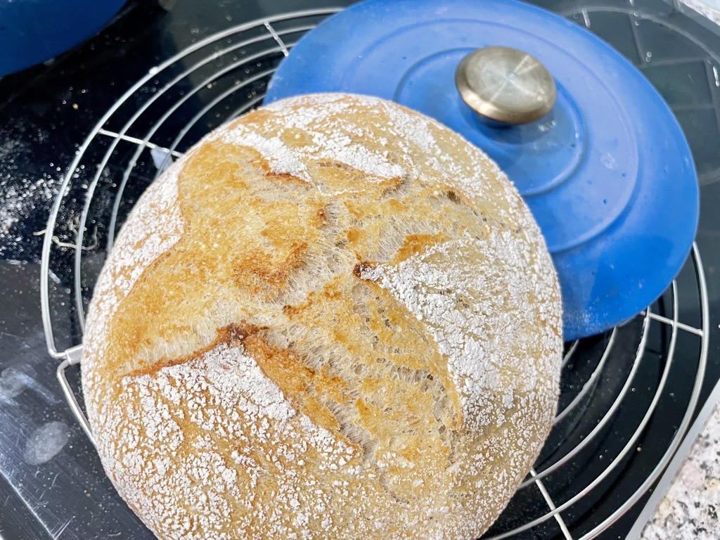 Round cooling rack with blue pot lid and sourdough loaf resting on it