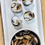 White platter with cream bowl of mushrooms next to four pieces of mushroom sushi